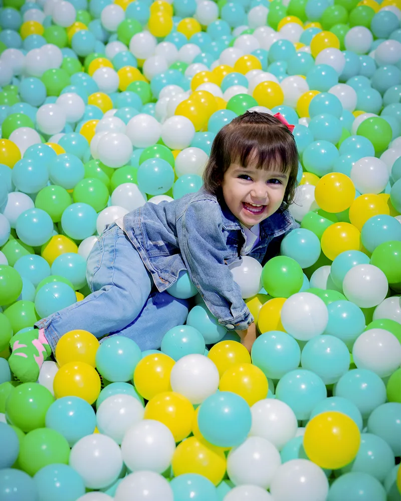 Niña sonriendo y jugando entre pelotas de colores en la piscina de Zuum Park