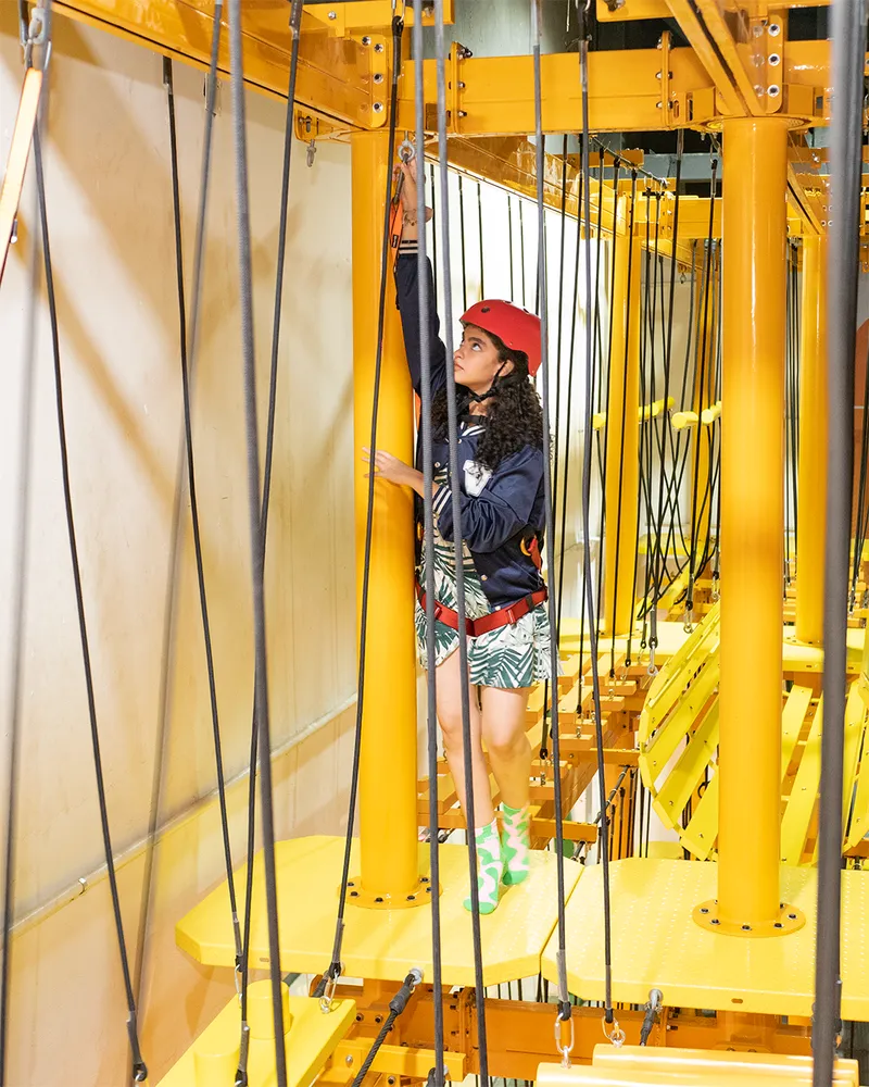 Joven con casco rojo escalando en el circuito de cuerdas de la Torre Zuum