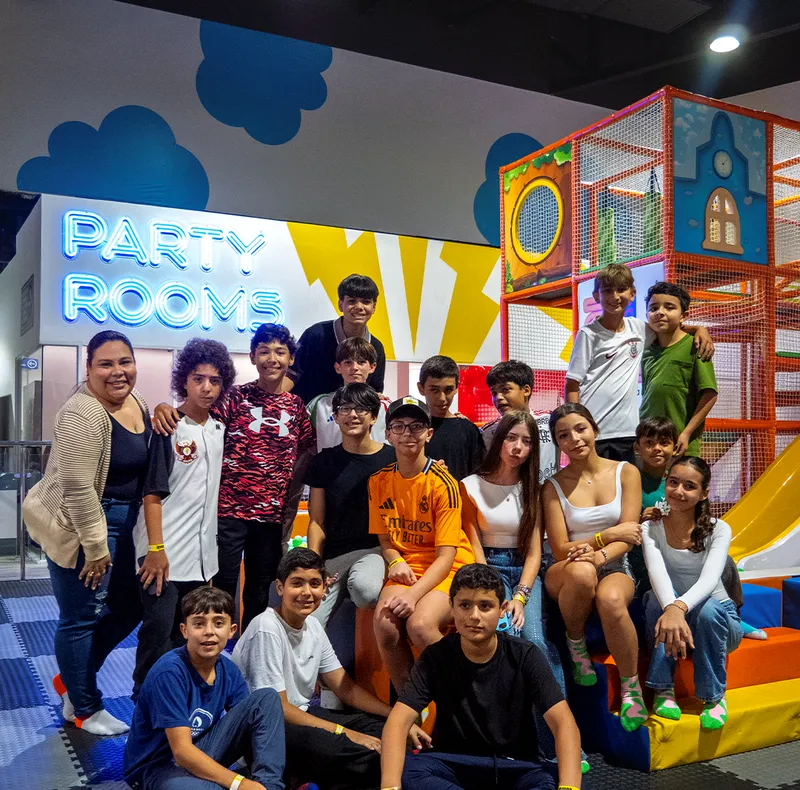 Grupo de jóvenes posando frente al área Party Room en Zuum Park