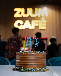 Torta de cumpleaños frente al letrero iluminado del Zuum Café