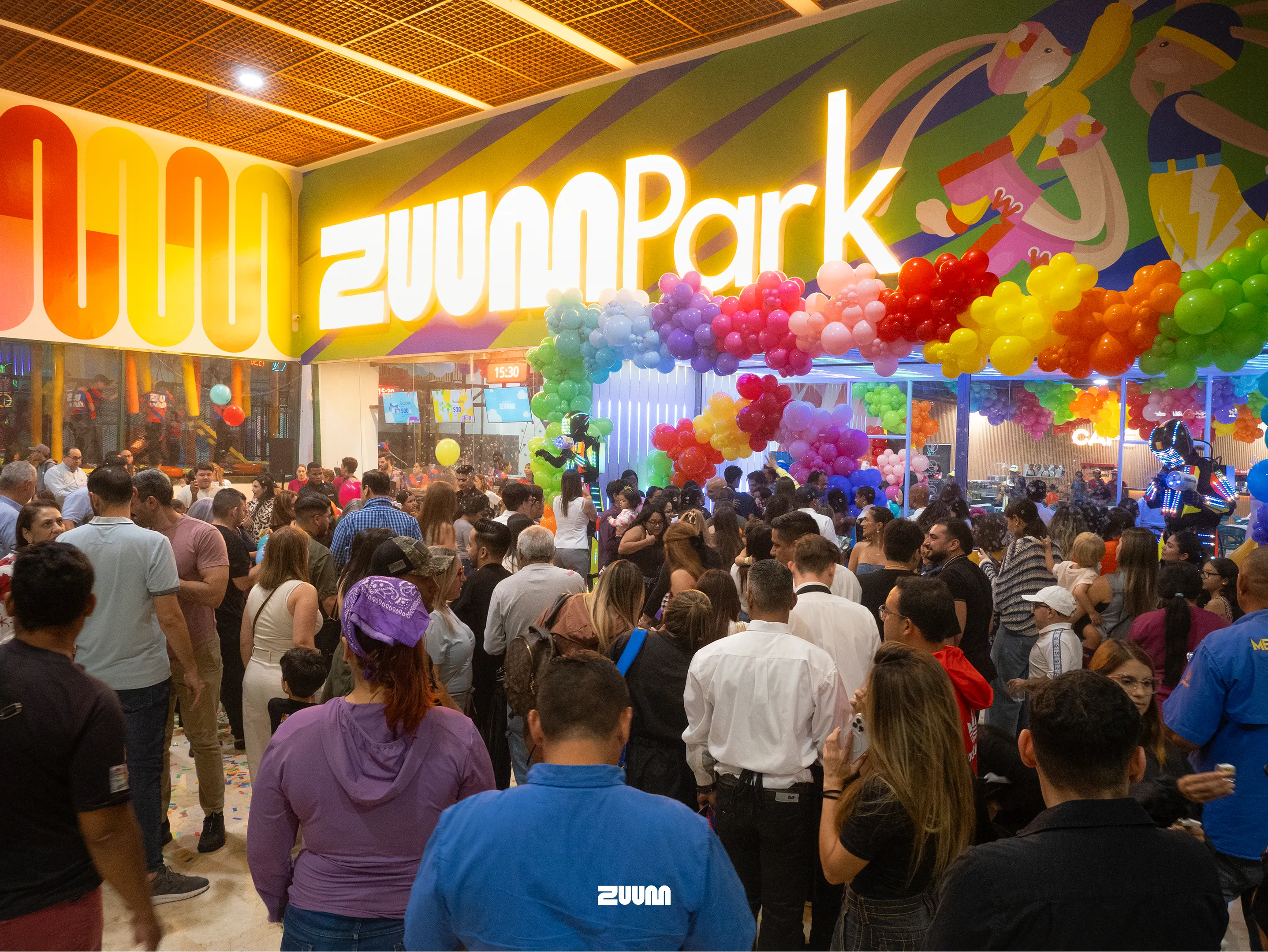 Gran multitud en la inauguración de Zuum Park, con letrero iluminado y arco de globos de colores